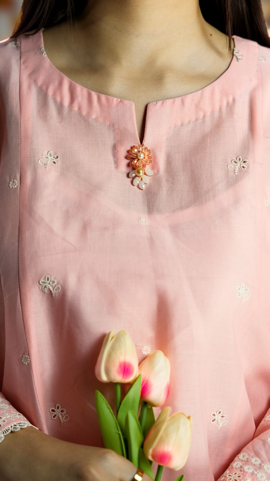 Person wearing a pink traditional outfit with floral embroidery, holding tulips.