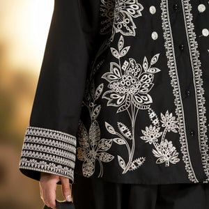 Person wearing a black outfit with white floral embroidery, holding a silver bag.