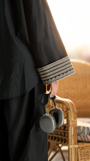 Person holding a gray bag with a textured surface, wearing a black garment with decorative cuffs.